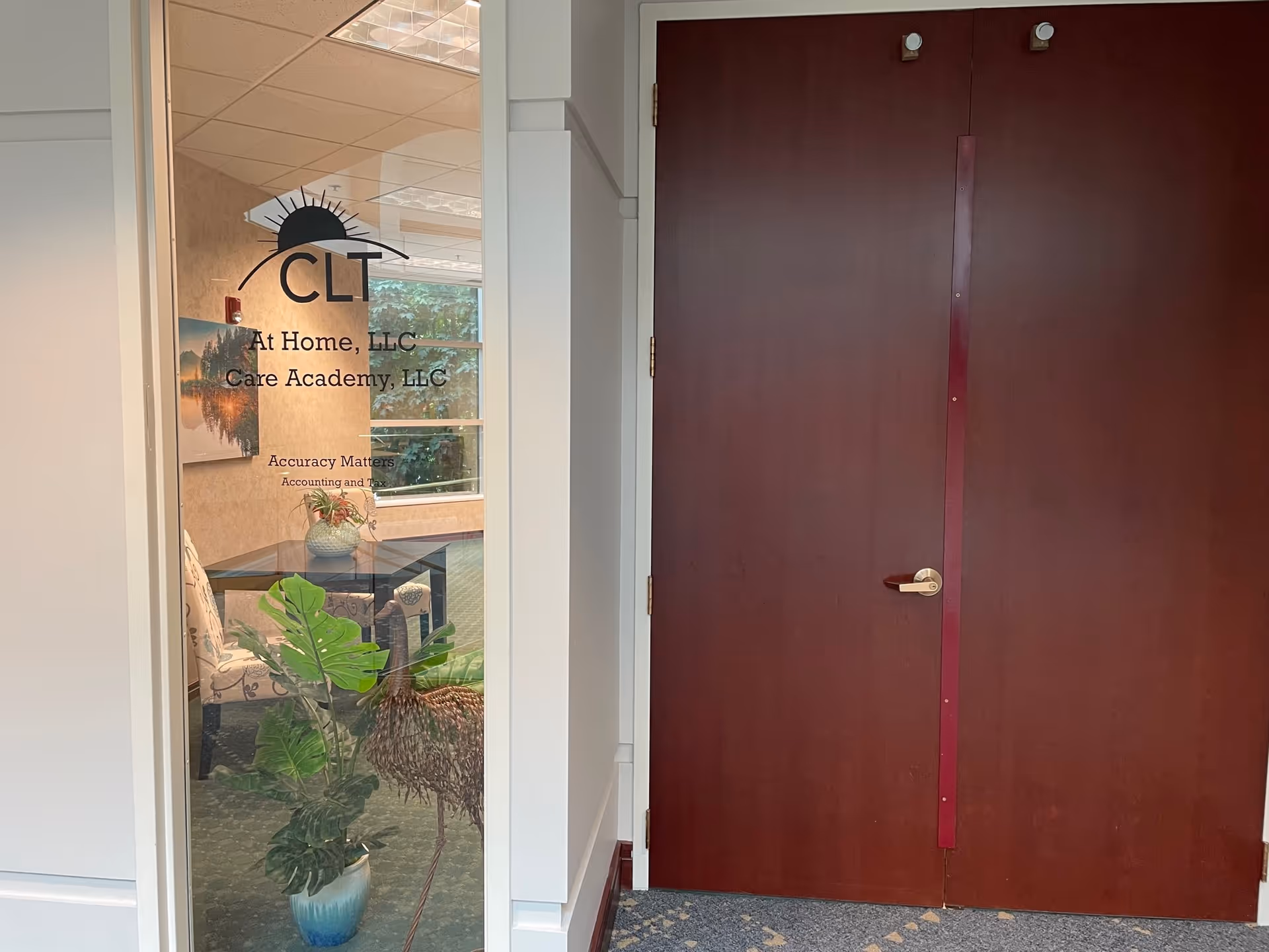 Glass door with CLT At Home, LLC signage, nearby plants visible in an interior hallway