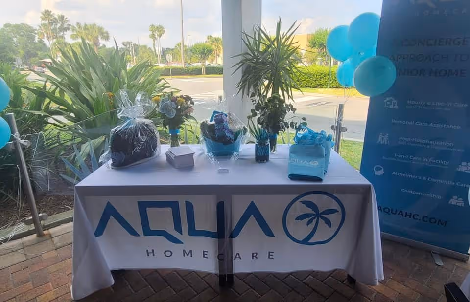 Table with Aqua Home Care banner, decorative plants, wrapped gifts, and balloons at the facility entrance.