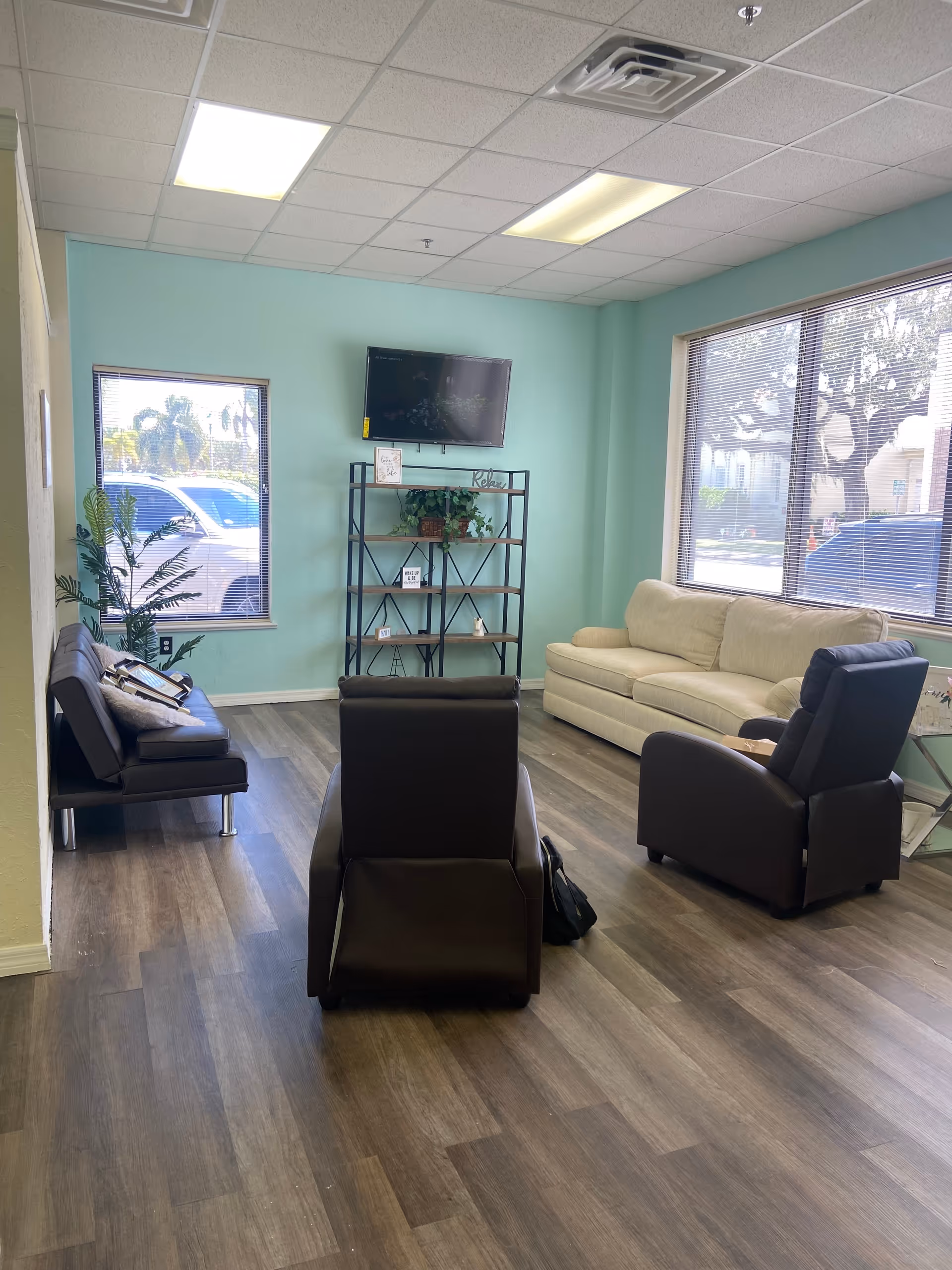 Bright waiting area with teal walls, seating, a TV, and large windows.