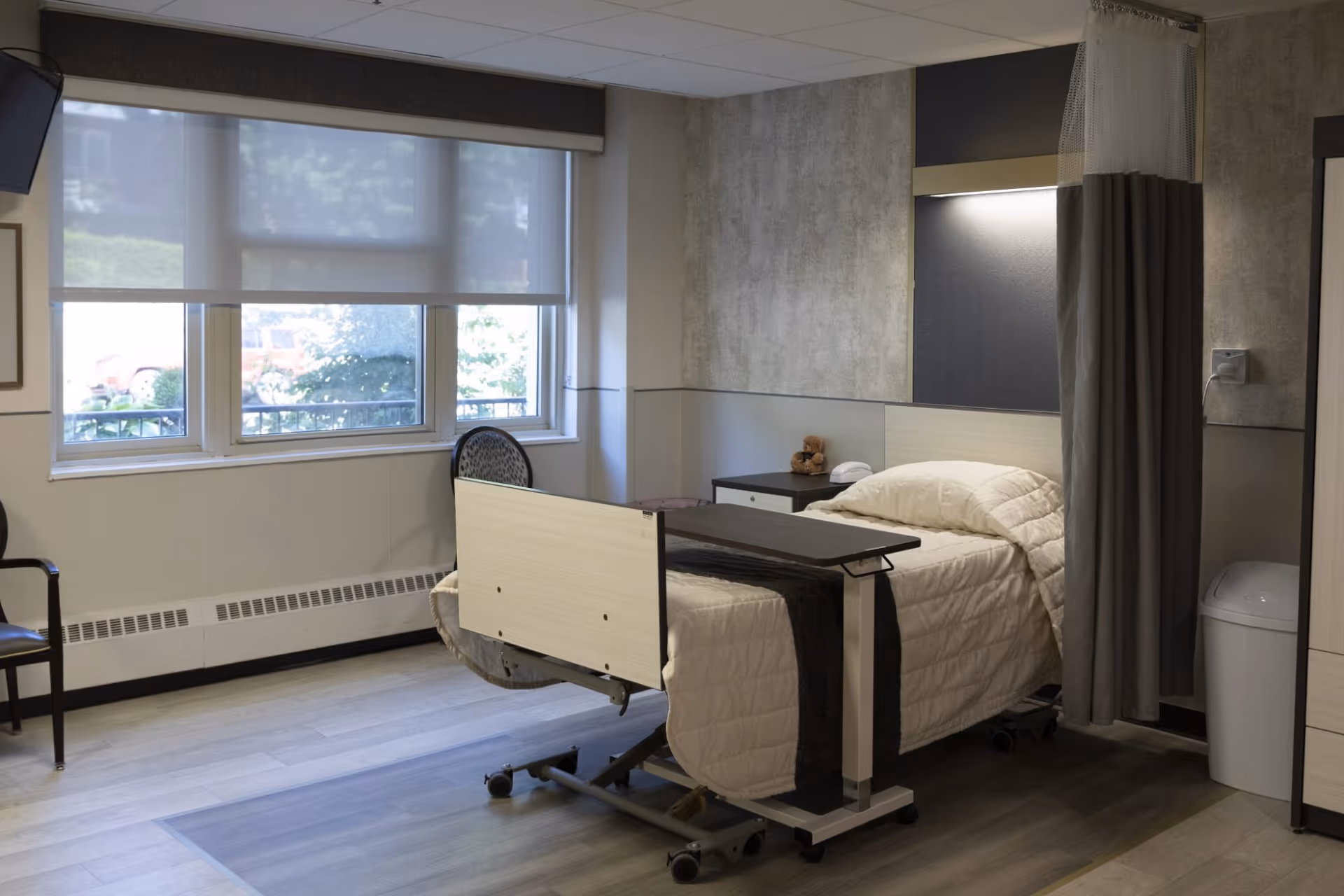 Hospital-style patient room with bed, privacy curtain, and window view.