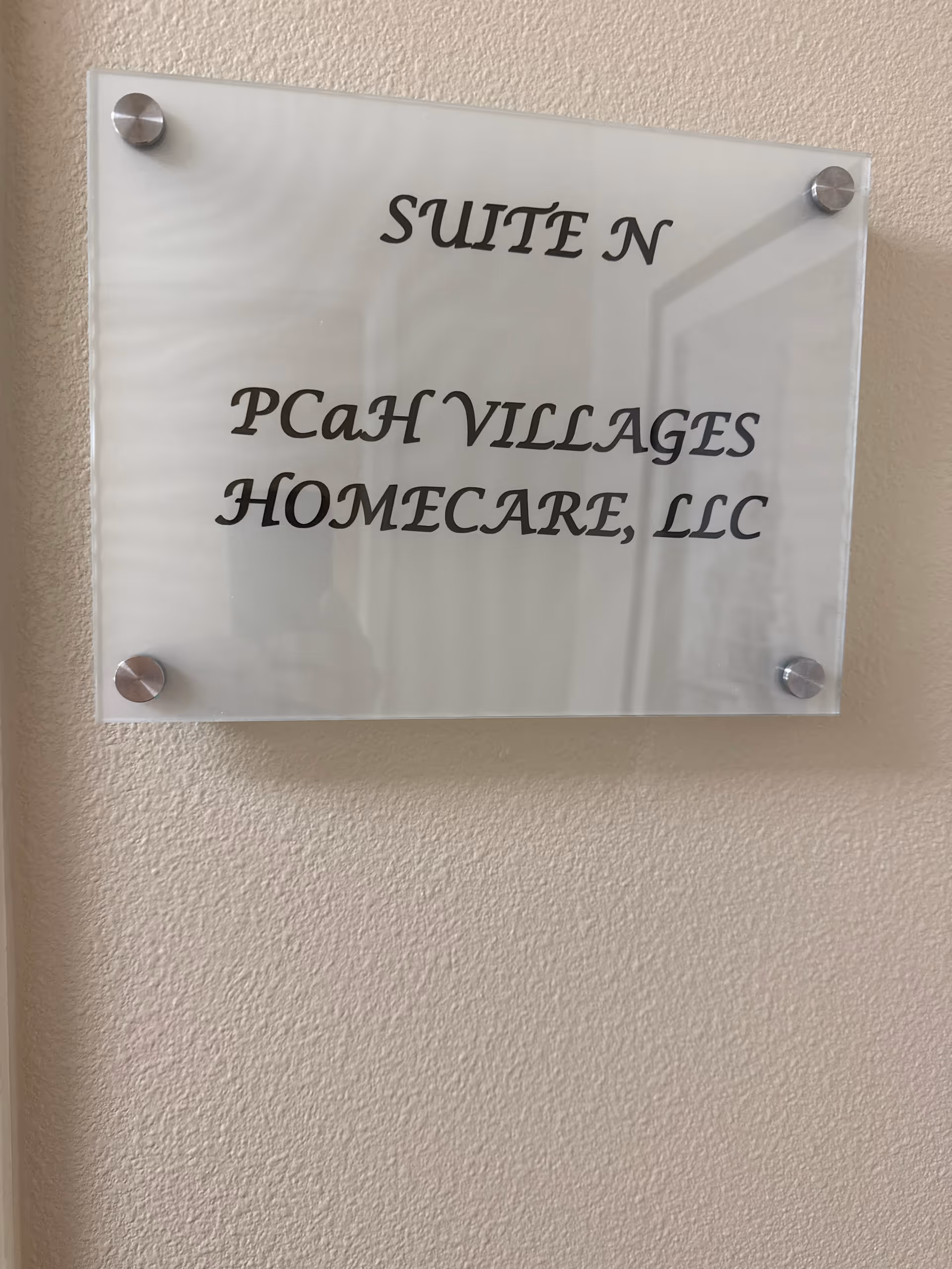 Glass plaque on a beige wall reads 'Suite N PCAH Villages Homecare, LLC'.