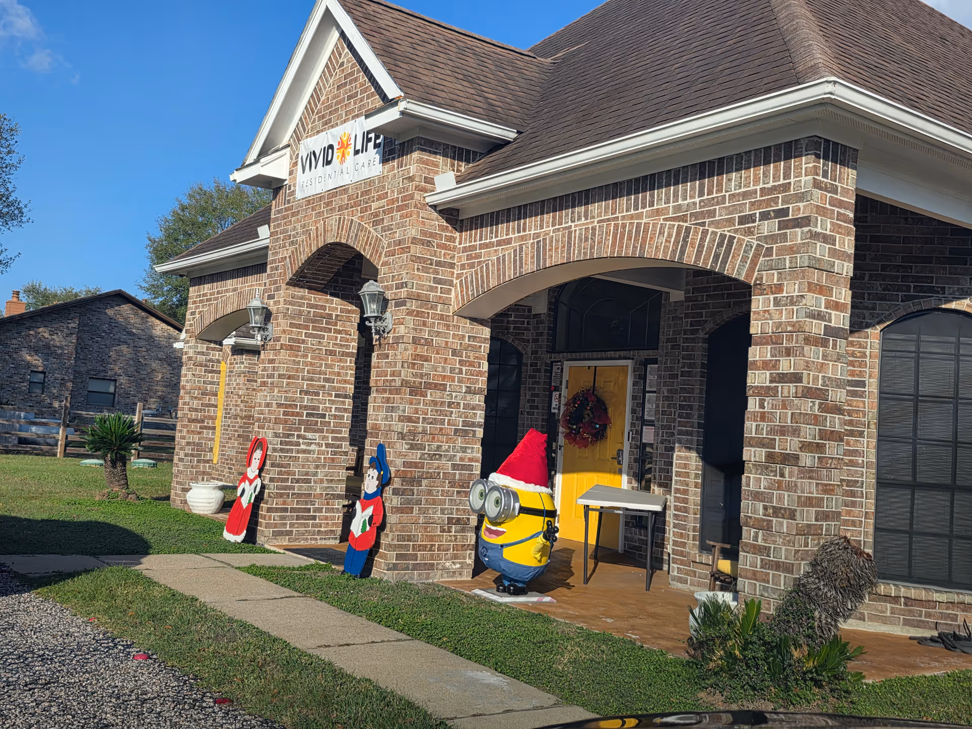 Brick senior living facility entrance with holiday decorations and a Minion figure.