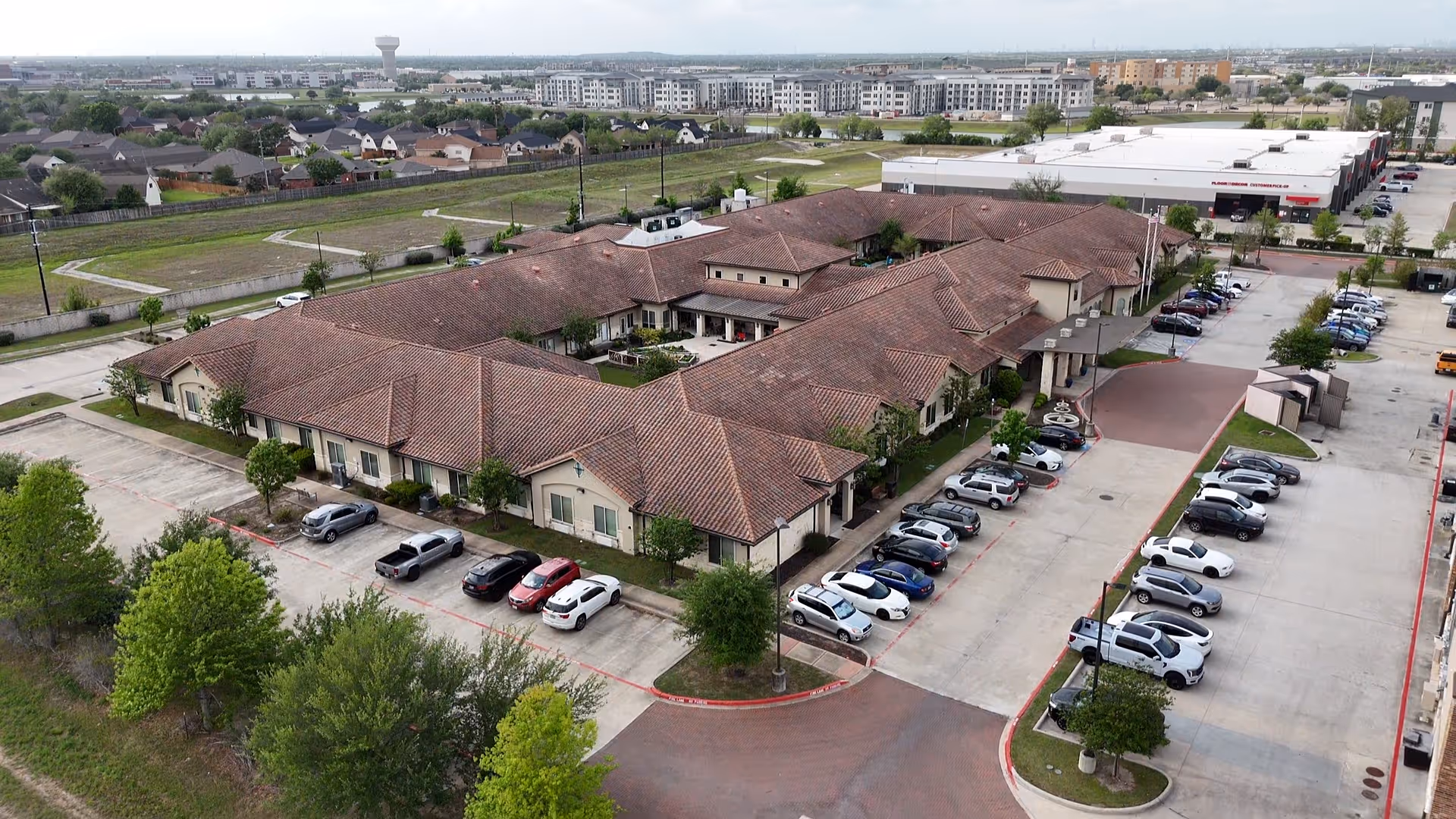 Aerial view of a senior living campus with brown-tiled roofs and parked cars.