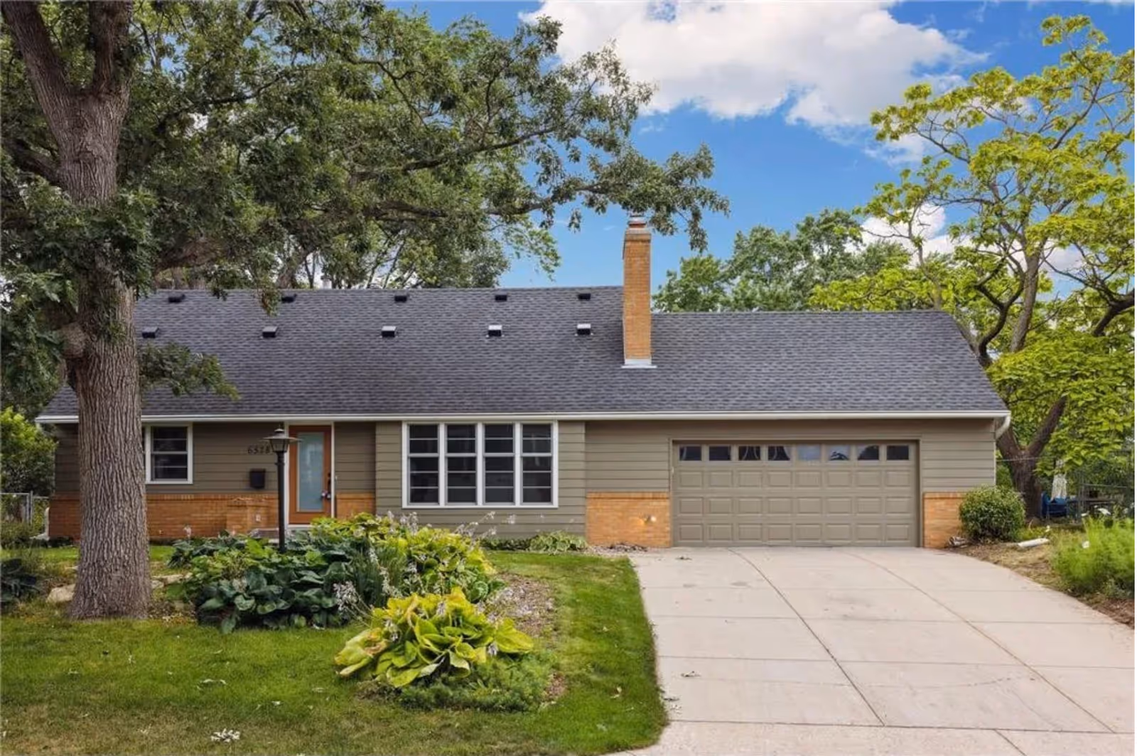 Single-story senior residence with a two-car garage, manicured yard, and large trees.