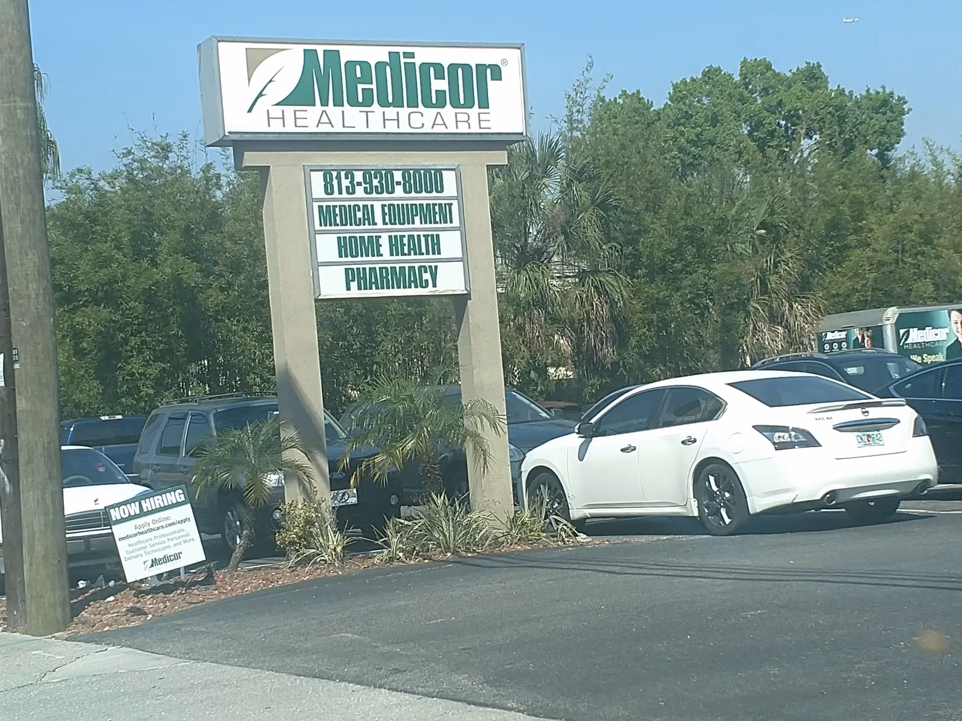 Medicor Healthcare sign atop pillar, with cars parked in a sunny lot.