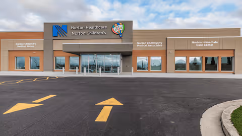 Exterior of Norton Healthcare building with glass entrance, signage, and parking.