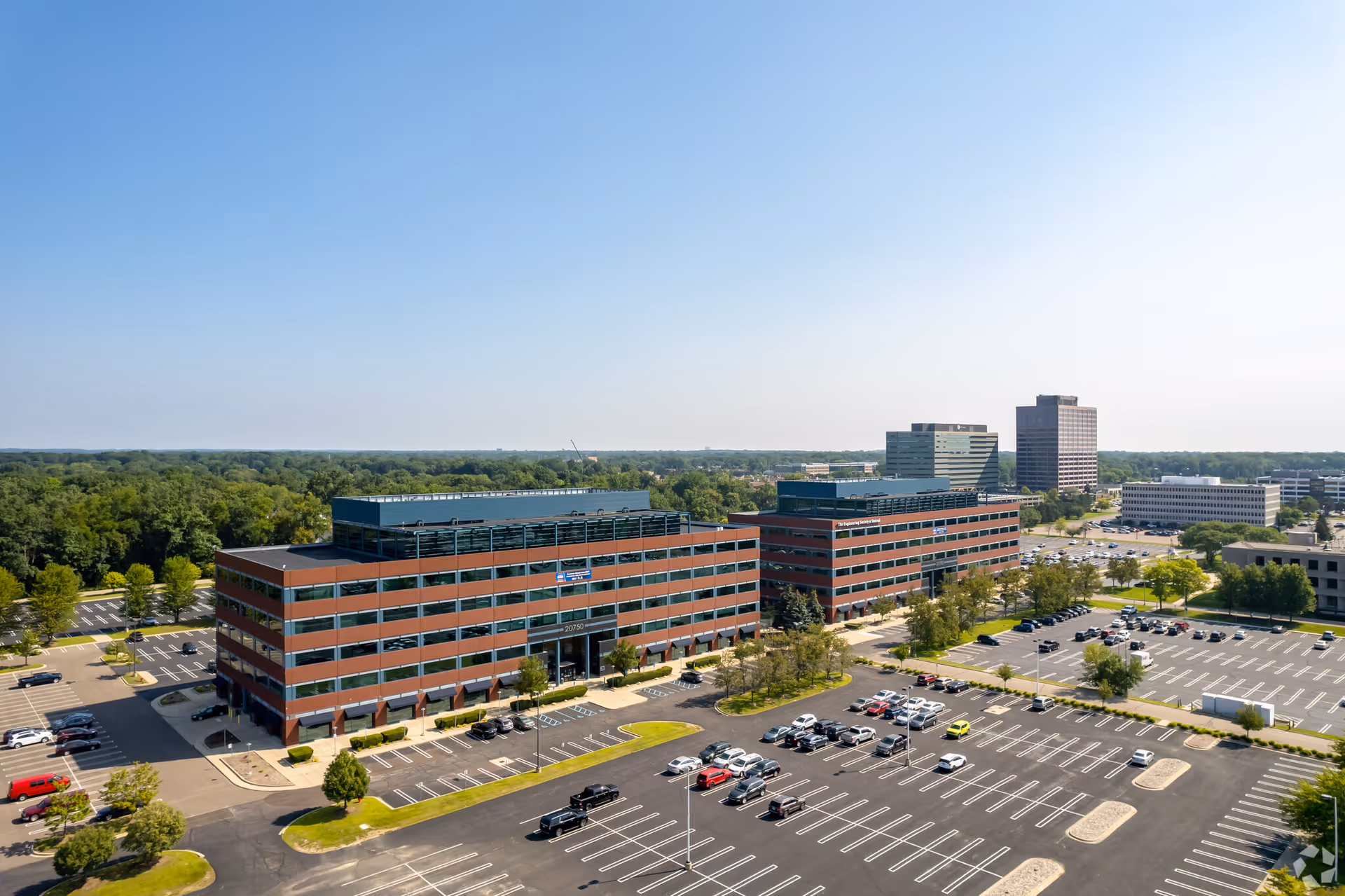 Aerial view of brick office complex with expansive parking and surrounding trees.