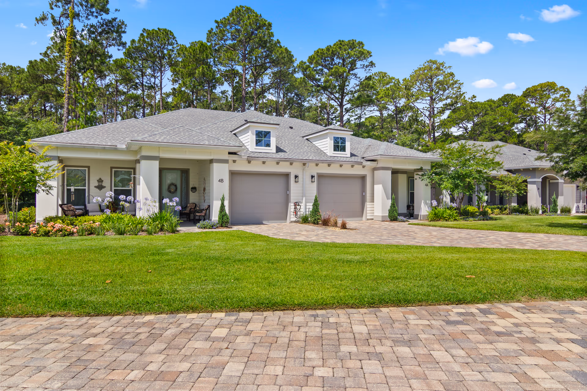 Row of modern single-story houses with garages, manicured lawns, and tall pine trees behind.