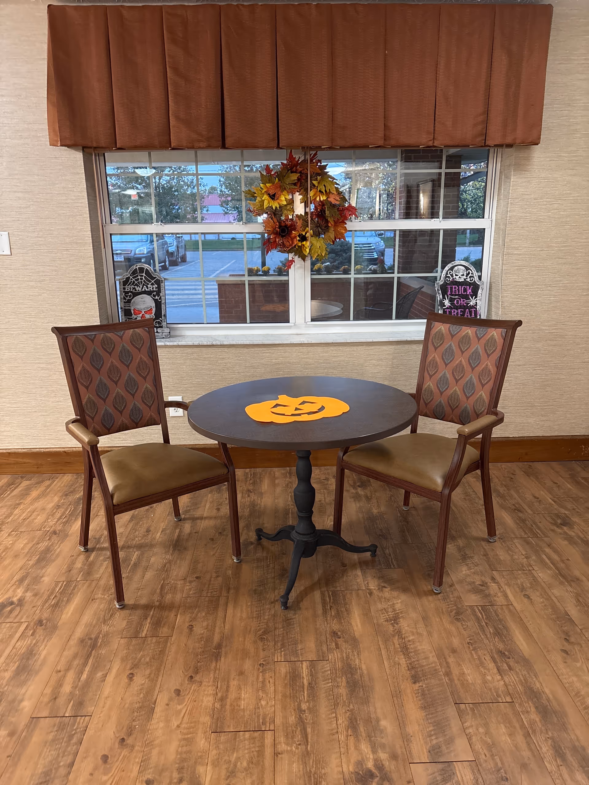Cozy dining nook with round table, two upholstered chairs, autumn decor, and pumpkin cutouts.
