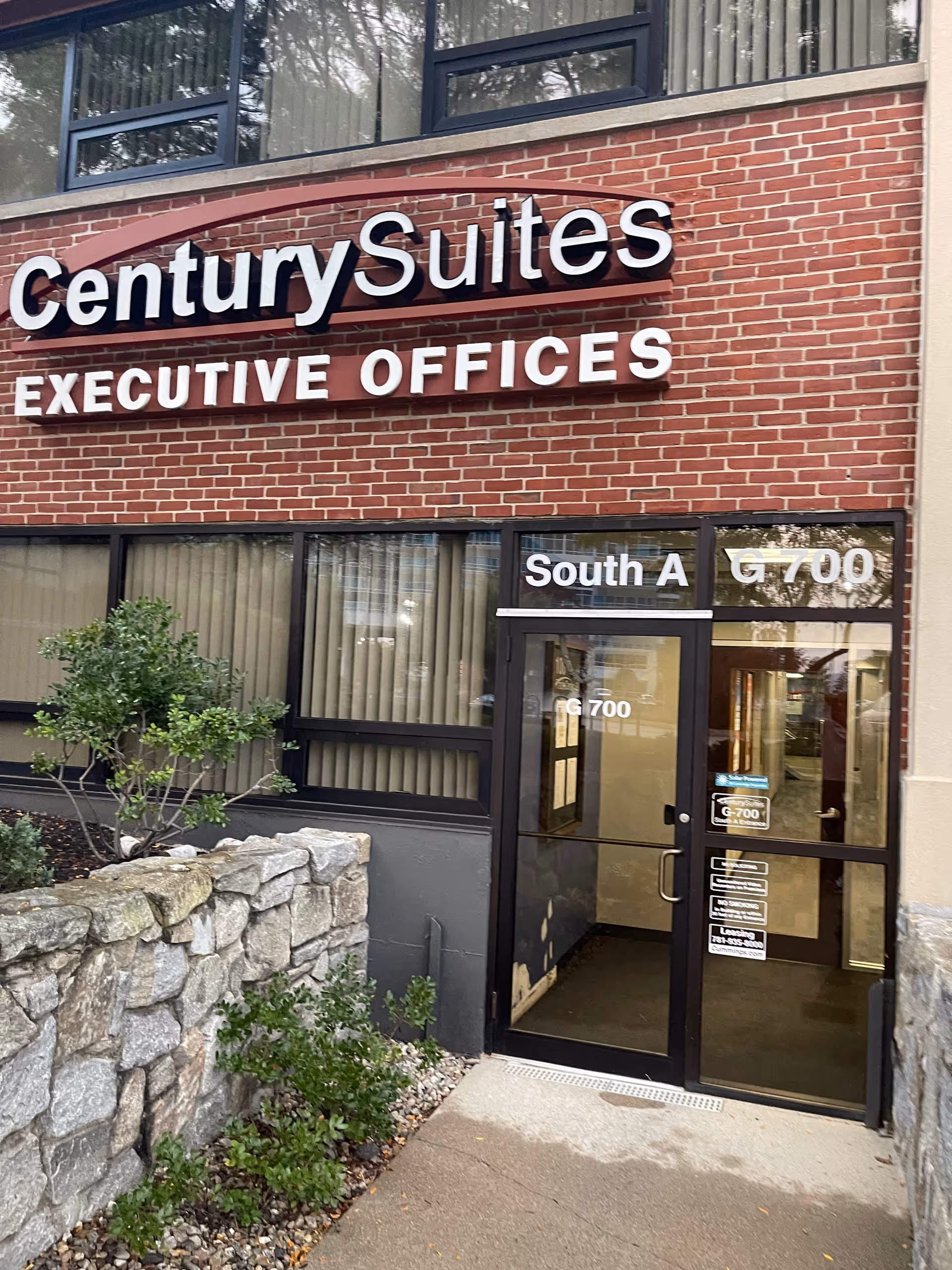 Brick building exterior with Century Suites Executive Offices sign and glass entrance.