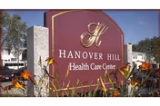 A maroon Hanover Hill Health Care Center sign with flowers in the foreground.