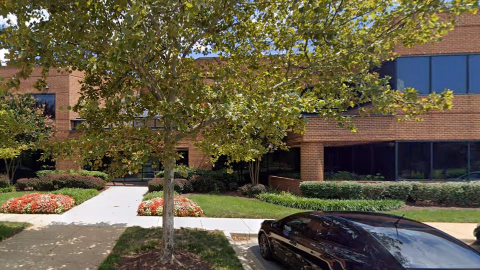 Exterior view of a brick senior care facility with landscaping, a tree, and a parked car.