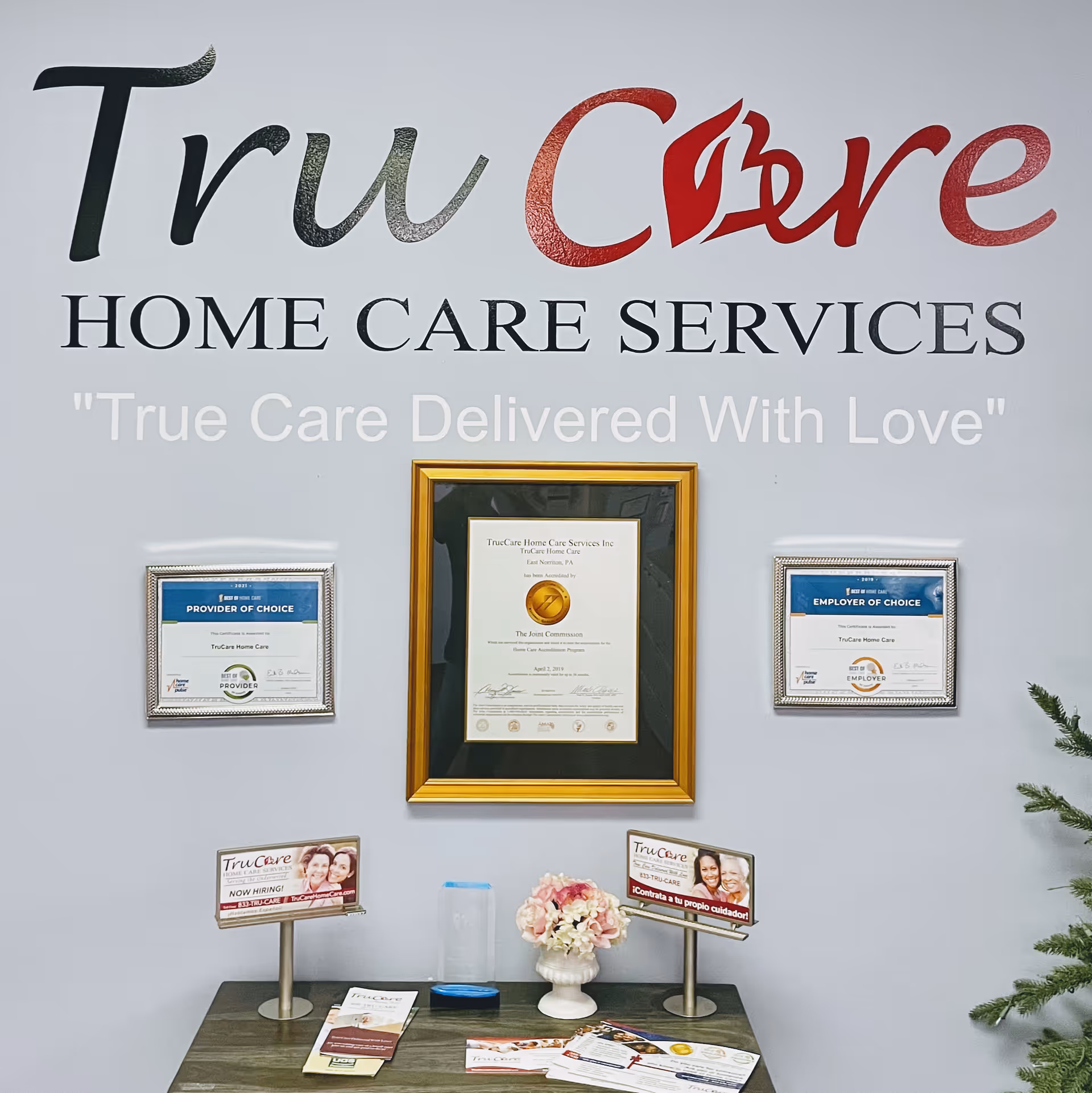 Interior lobby wall displays TruCare Home Care Services sign with framed certificates and brochures