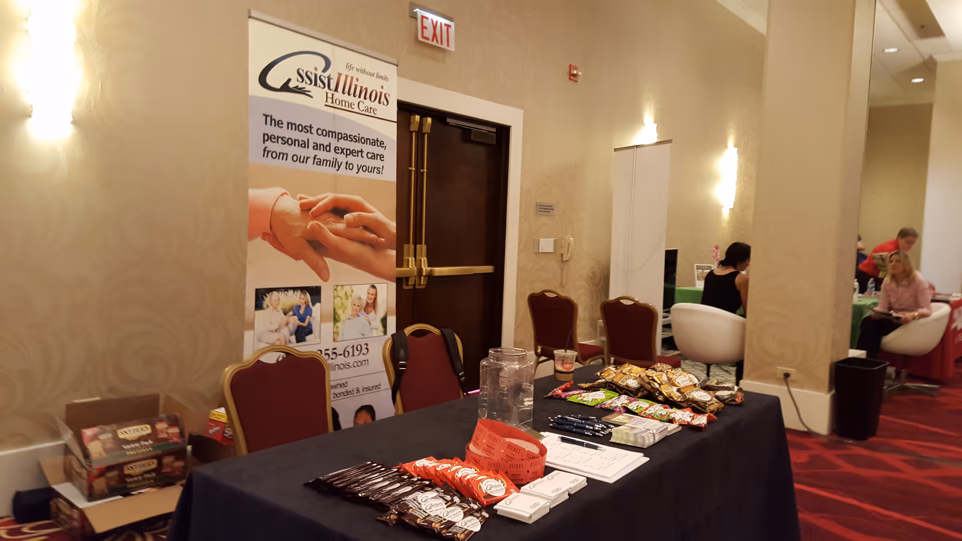 Indoor event setup in a beige hallway with a promotional banner and snack table.