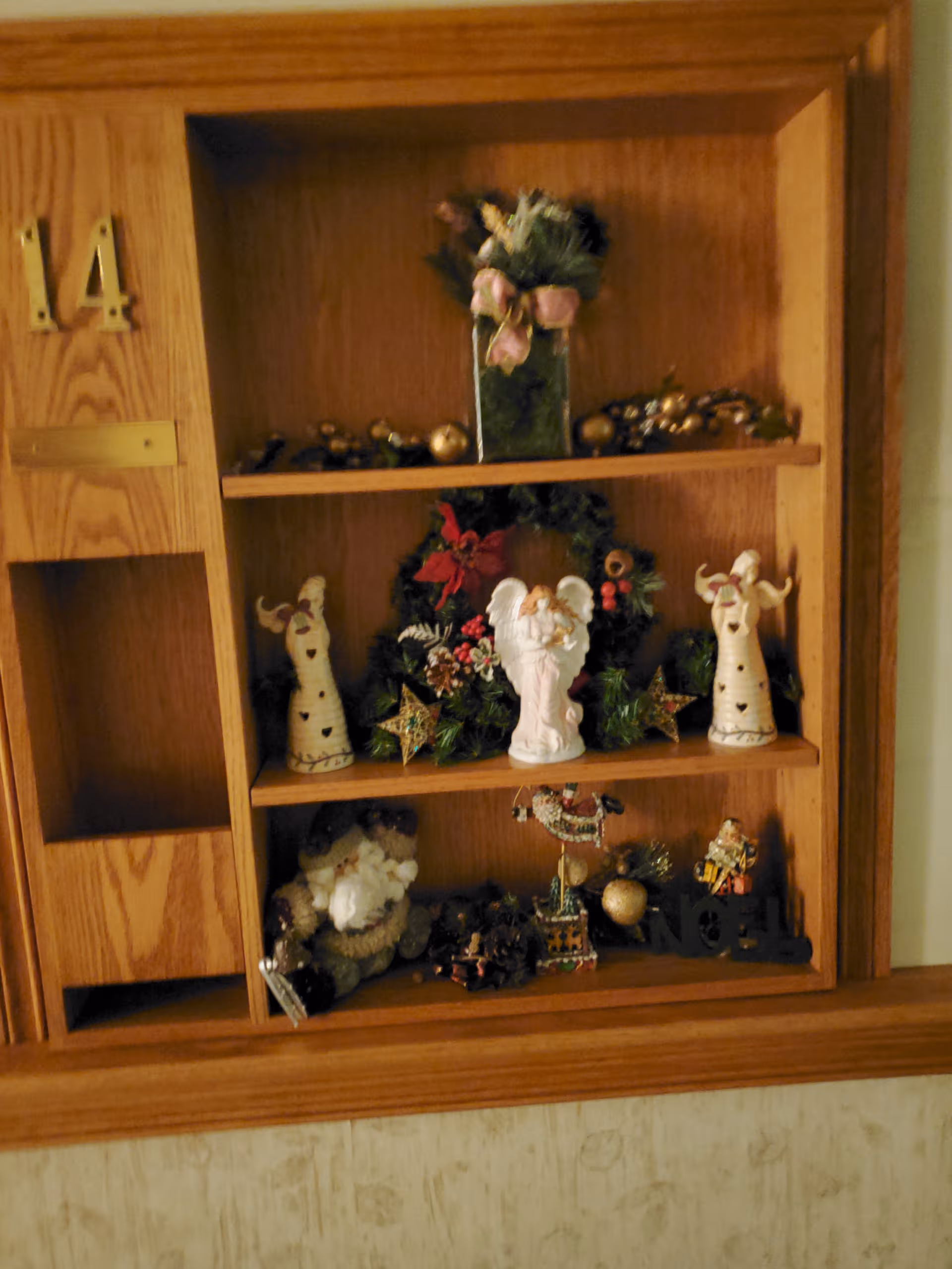Wooden wall cabinet with holiday decor and angel figurines on shelves.