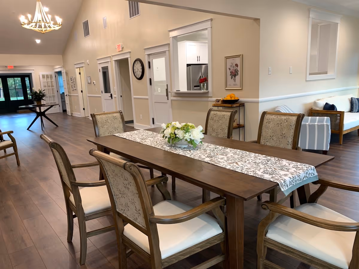 A long wooden dining table with a floral centerpiece in a senior living dining room.