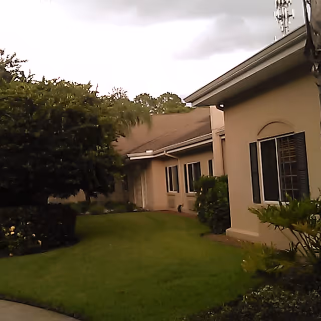 Exterior view of a beige senior living building with a manicured lawn and shrubs.