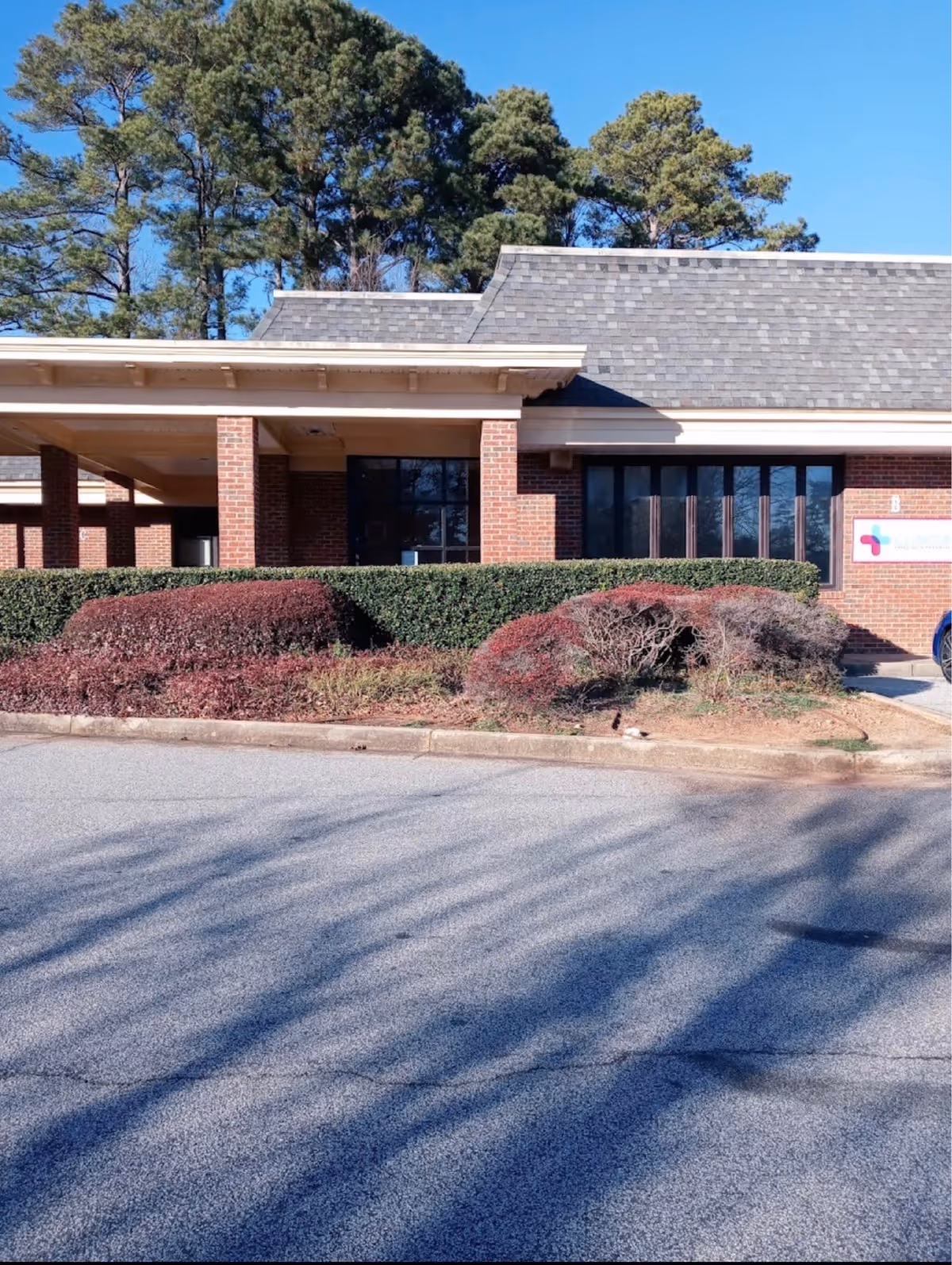 Brick medical facility exterior with hedges, large windows, and a blue sky.