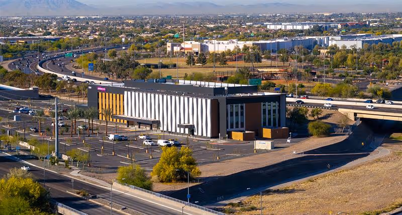 Aerial view of a modern medical campus building, highway, parking lot, and distant mountains.