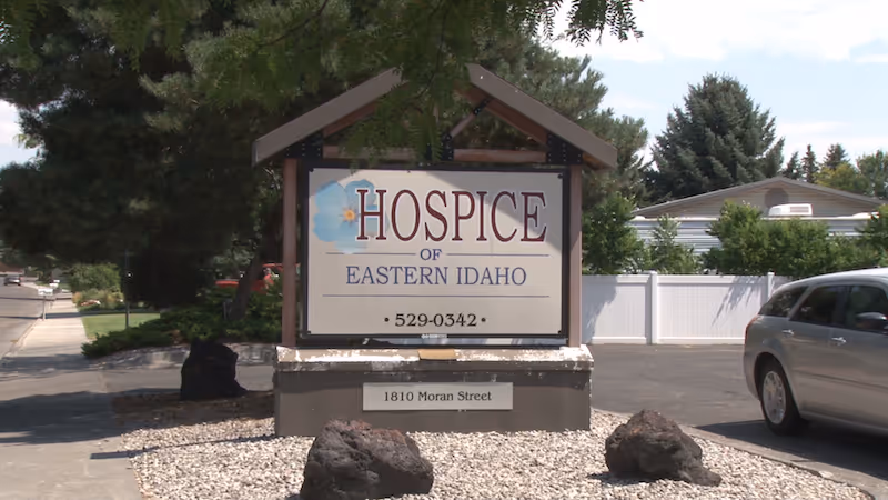 Outdoor sign for Hospice of Eastern Idaho beside a parking lot and landscaping.