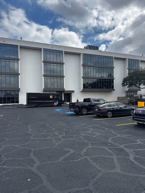 Front exterior of a white, multi-story building with large windows and a parking lot.