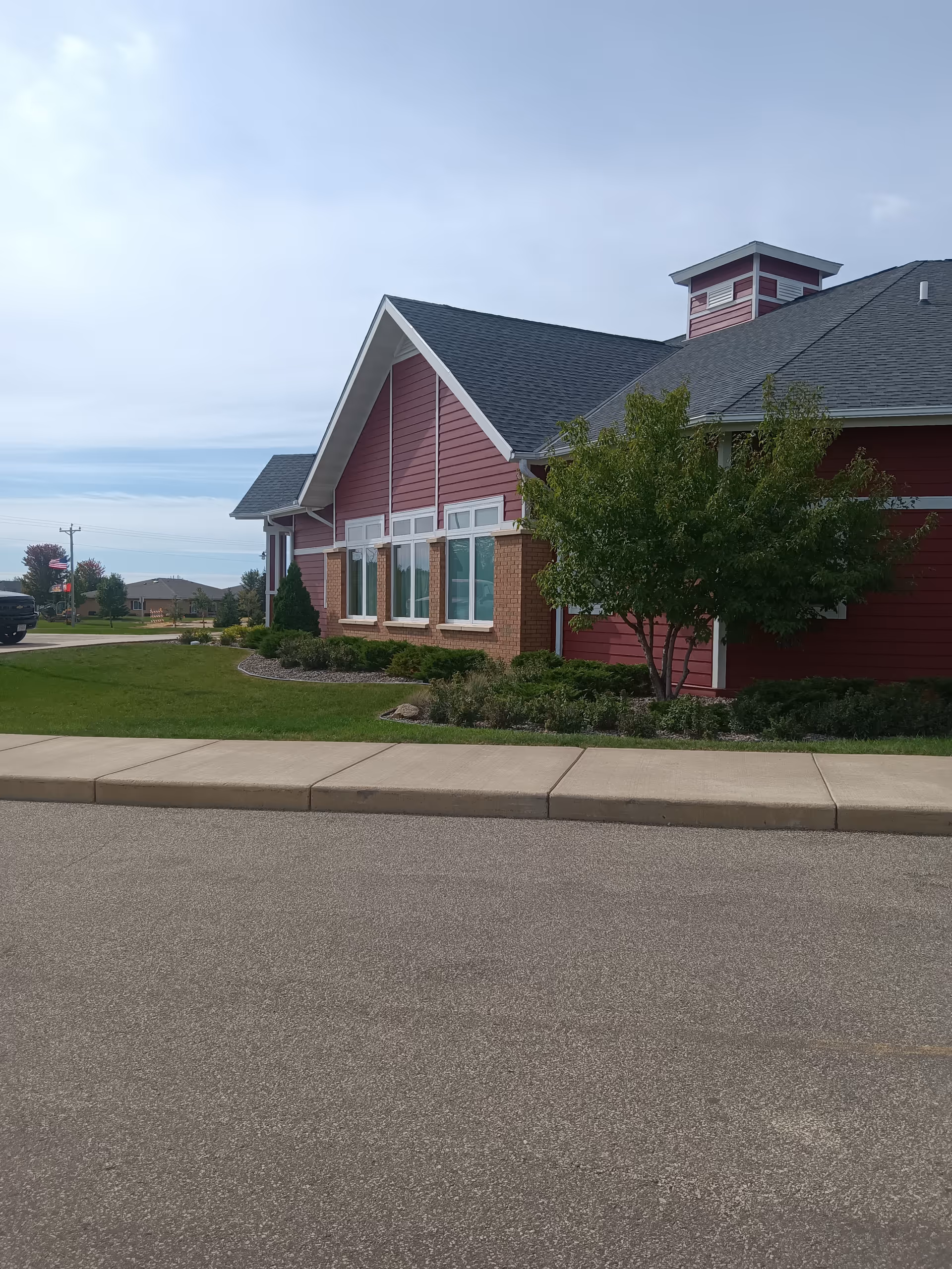 Exterior view of a red siding memory care center with windows and landscaped surroundings.