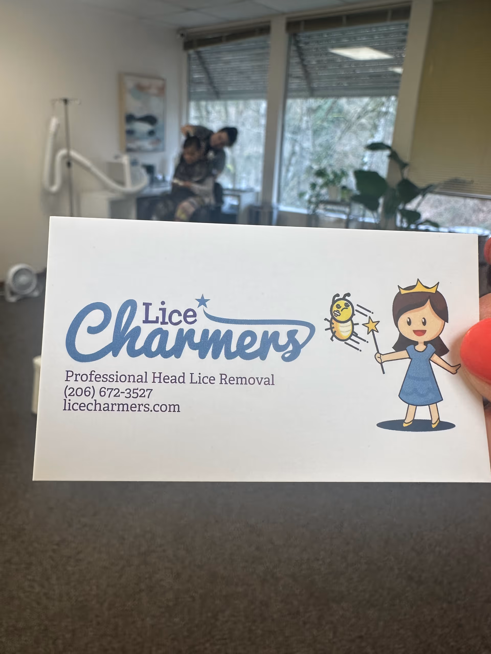 A Lice Charmers business card is held up in a senior living facility lobby or lounge.