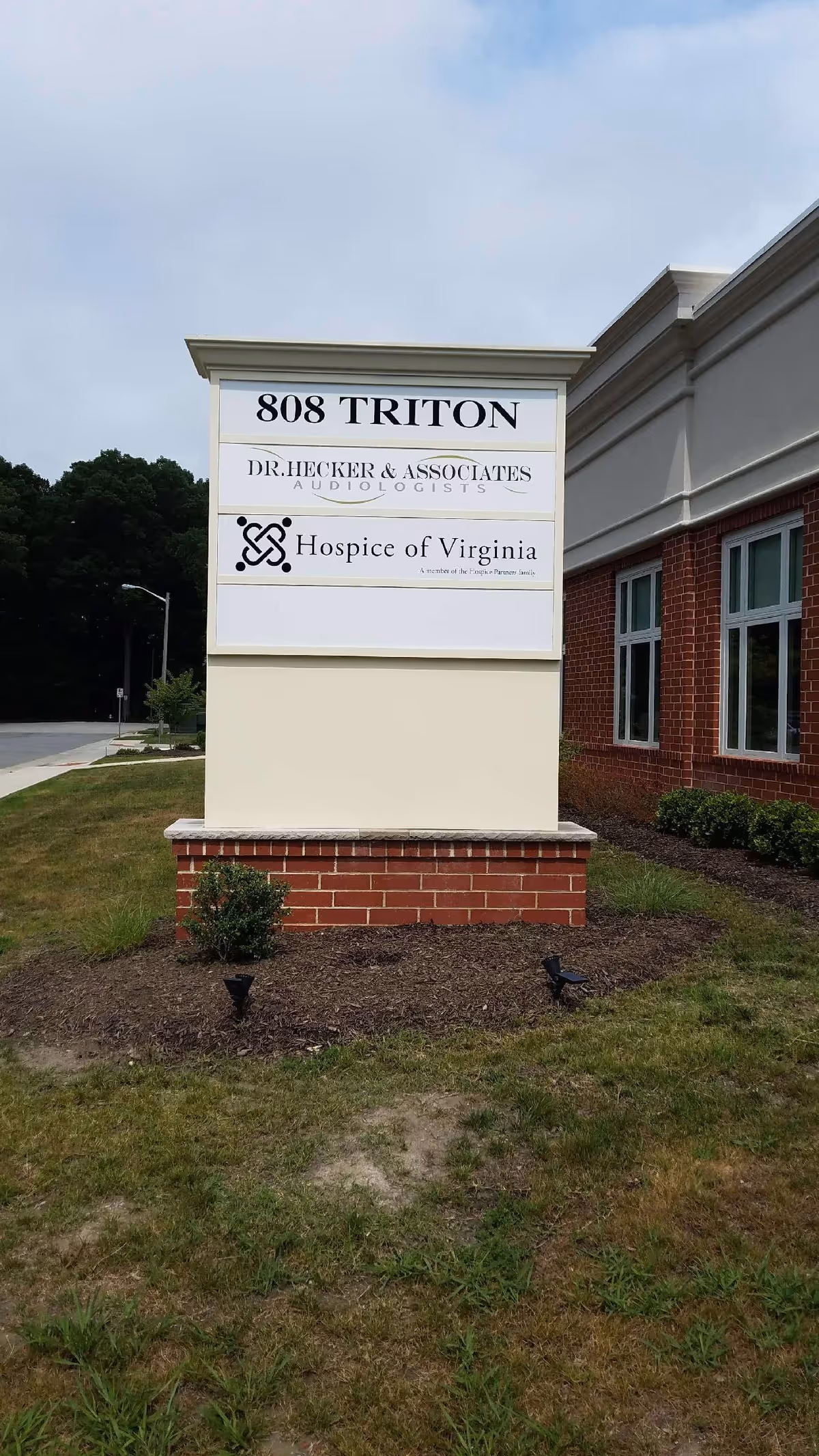 A tall exterior sign near a brick building reads Hospice of Virginia and 808 Triton.