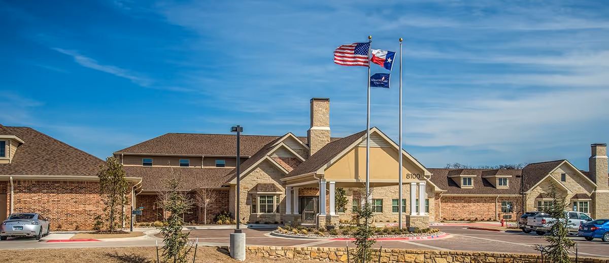 Exterior view of Ellery Arbor senior living facility with flags and entrance.