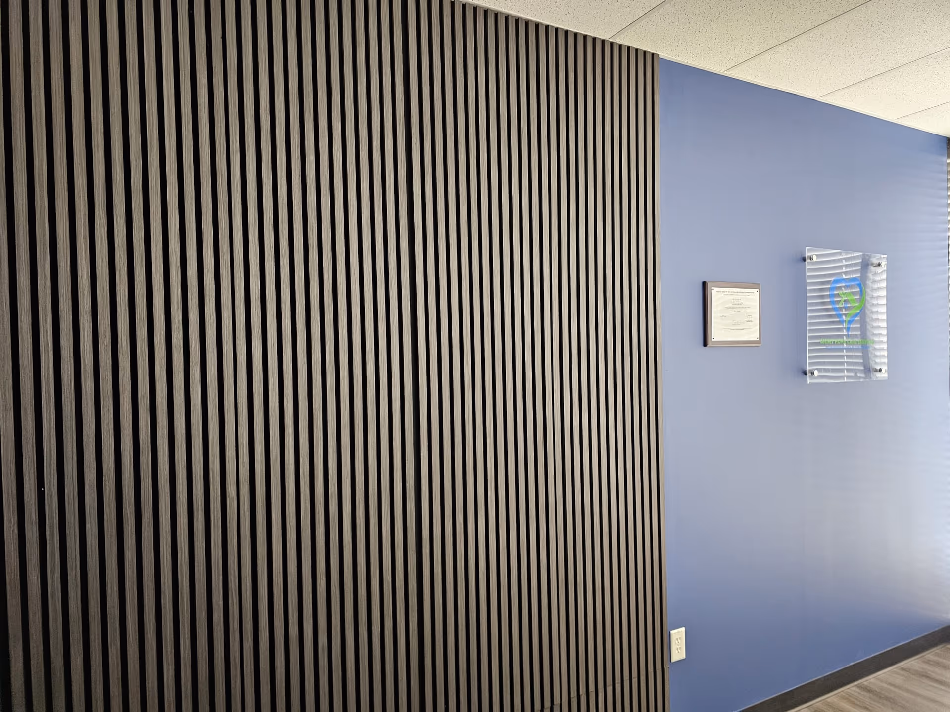 Interior hallway with black vertical slats on left and blue wall with plaques.