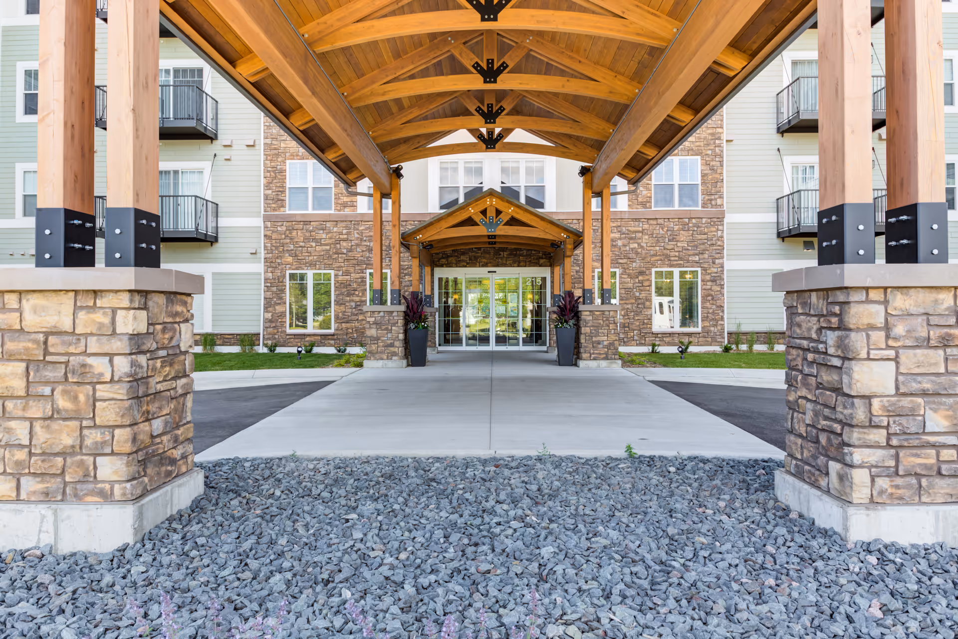 Front entrance of a senior living facility with a wooden porte-cochère and stone pillars.