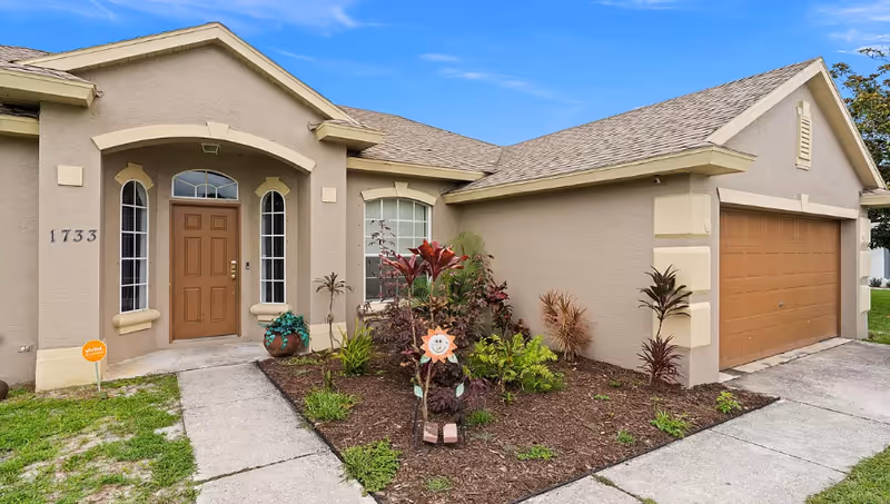 Single-story beige building with brown front door, two-car garage, and landscaped front yard.