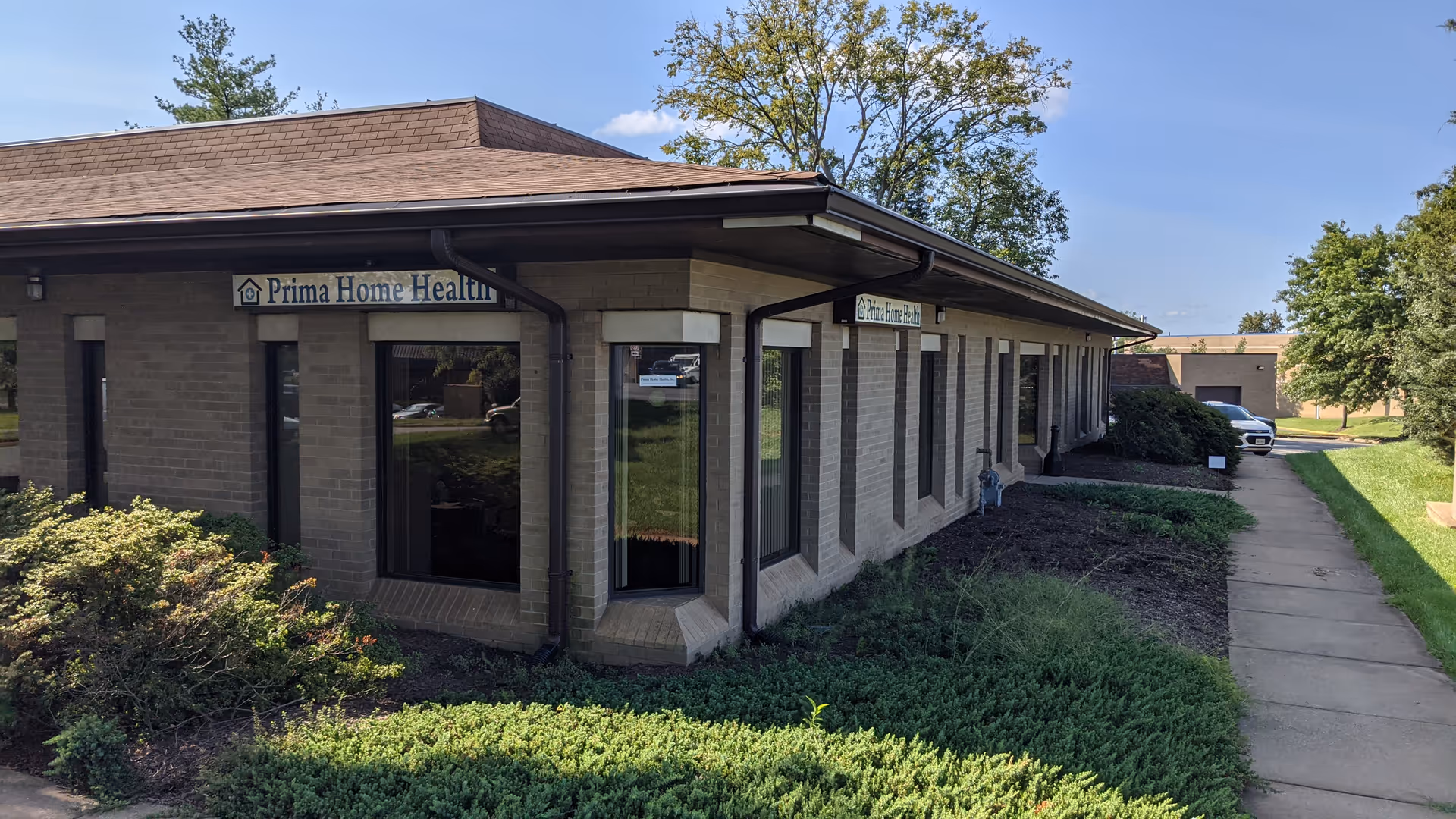 Single-story brick building labeled Prima Home Health with windows and a sidewalk.