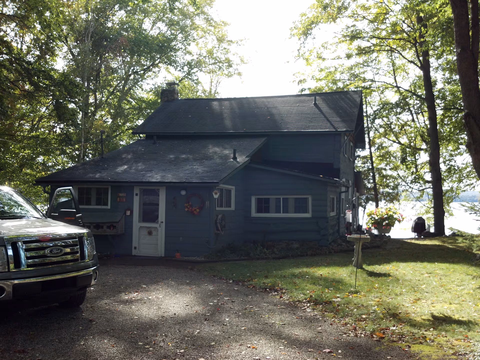 A blue log home exterior with a truck beside trees by the water.