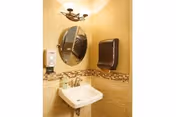 Small bathroom sink area with mirror, soap dispenser, and tiled walls.