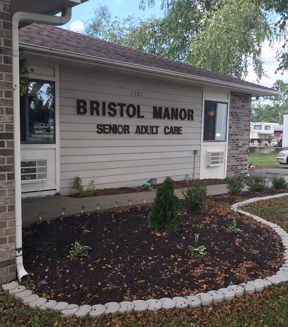 Front exterior of Bristol Manor Senior Adult Care with landscaping and a sign