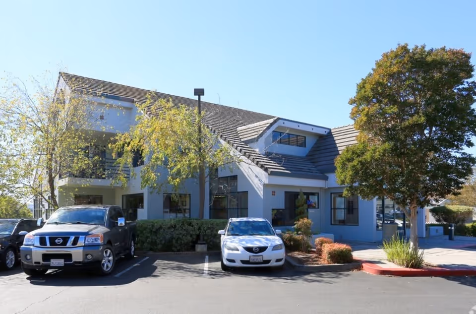 A light-blue senior living facility building with cars in a parking lot.