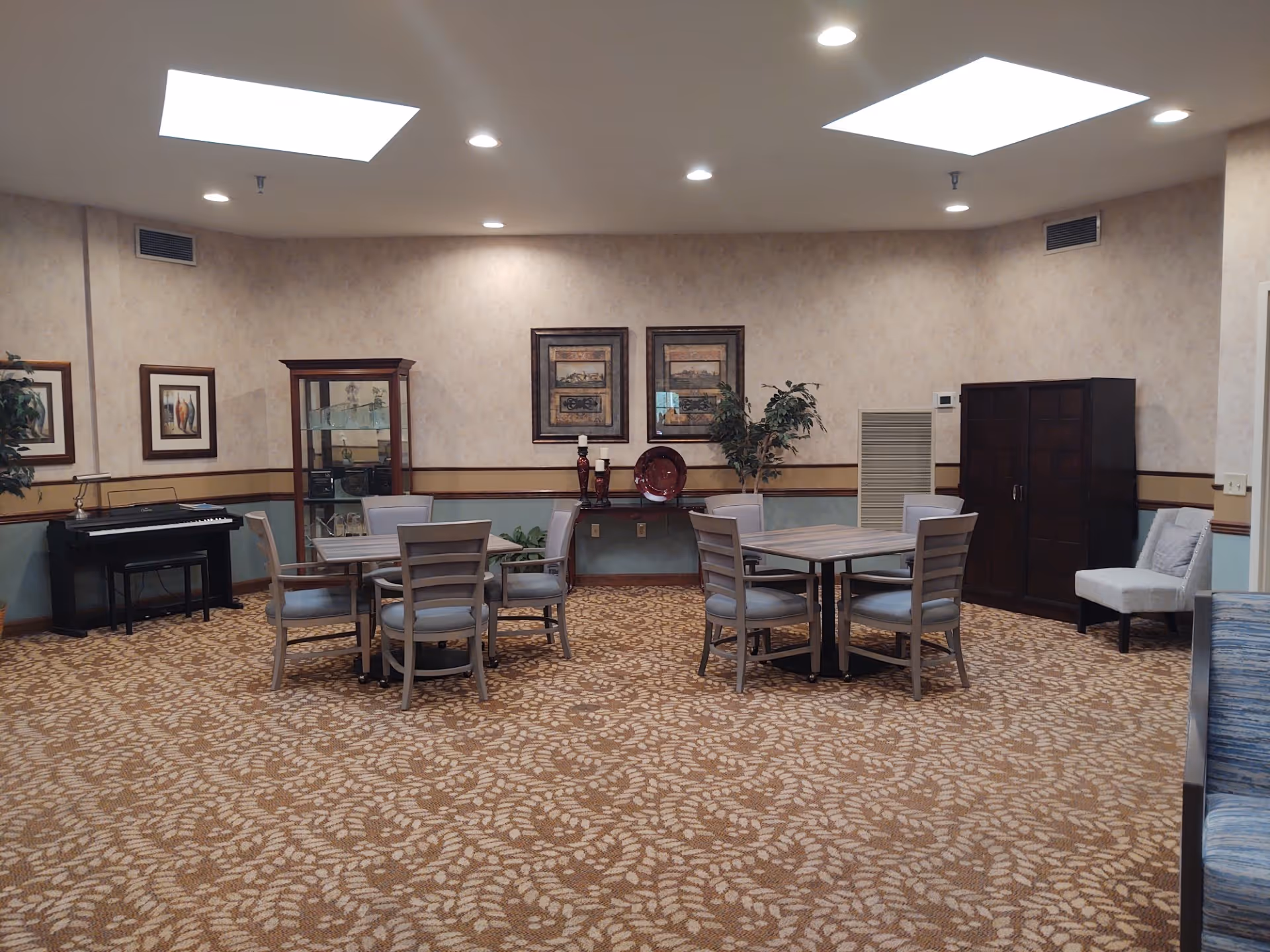 Public lounge area with round tables, chairs, piano, and wall art.