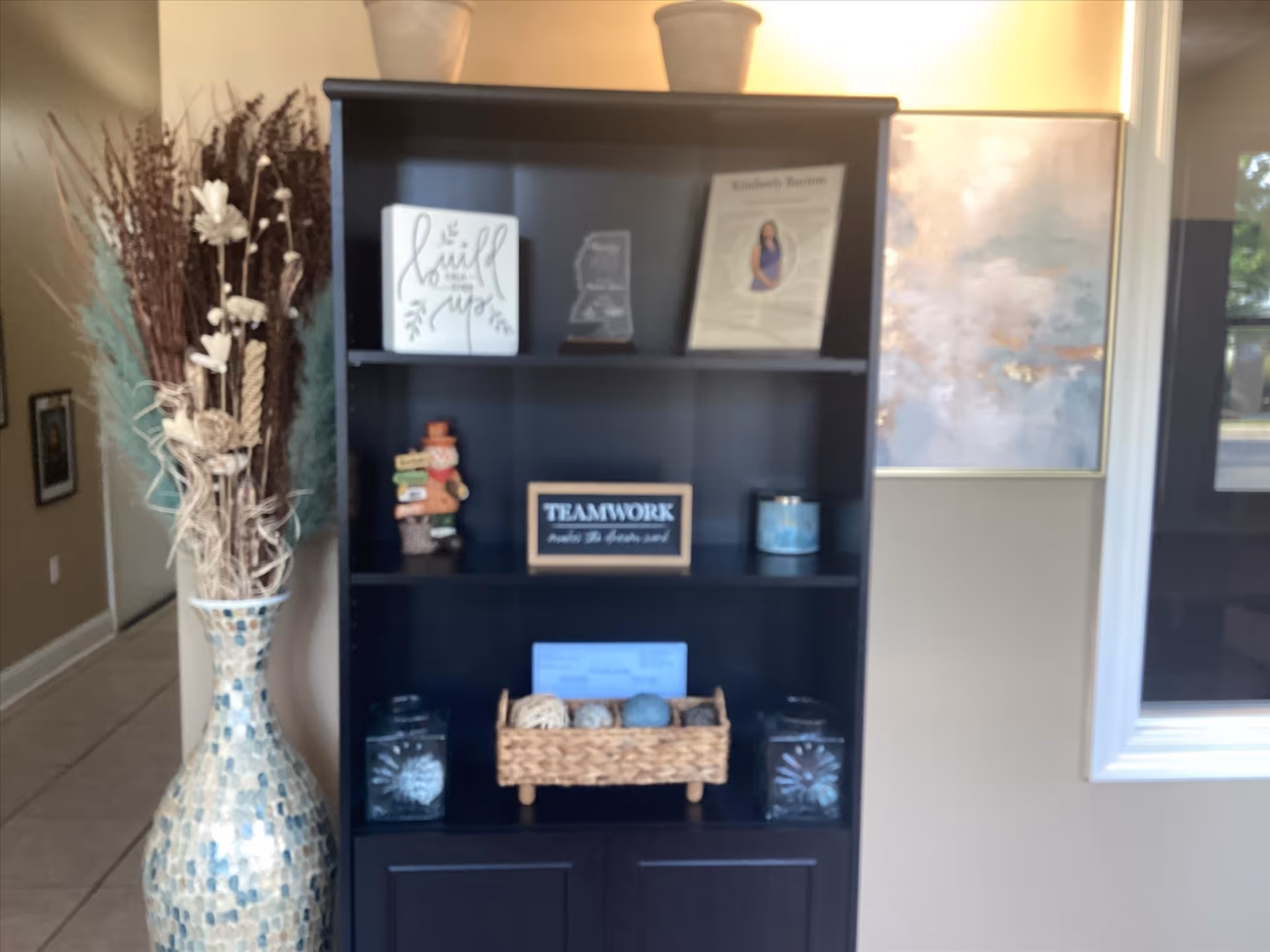 Tall dark bookshelf with decor, vase, and map on wall in a lobby area.