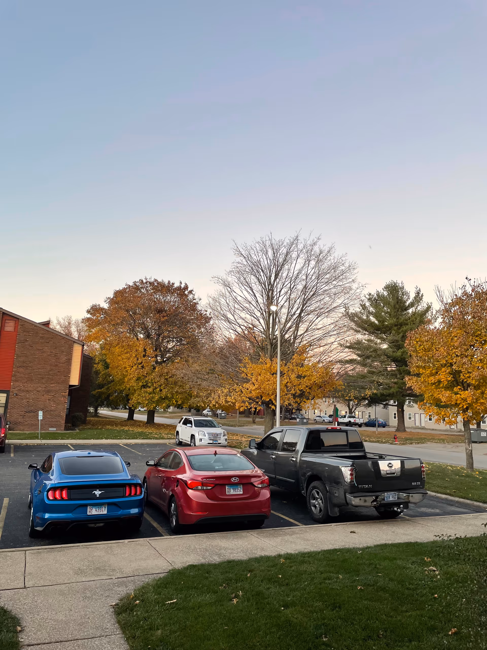 Parking lot with blue, red, and black cars in front of a brick facility during autumn.