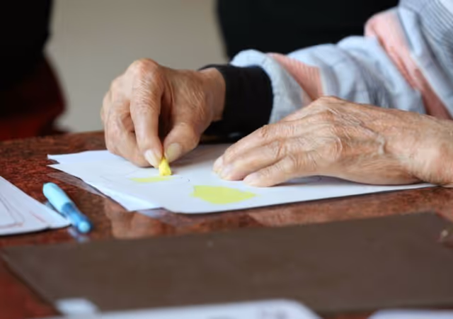 Close-up of elderly hands using a yellow highlighter on papers at a table.