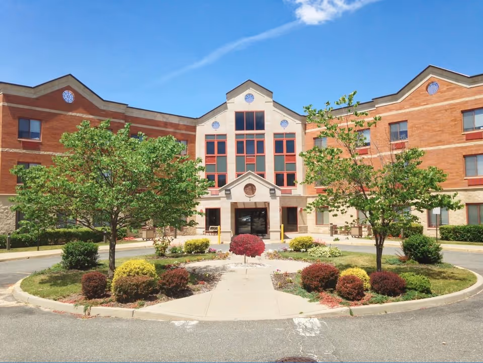 Front exterior of a three-story brick senior living facility with a landscaped circular driveway and main entrance.