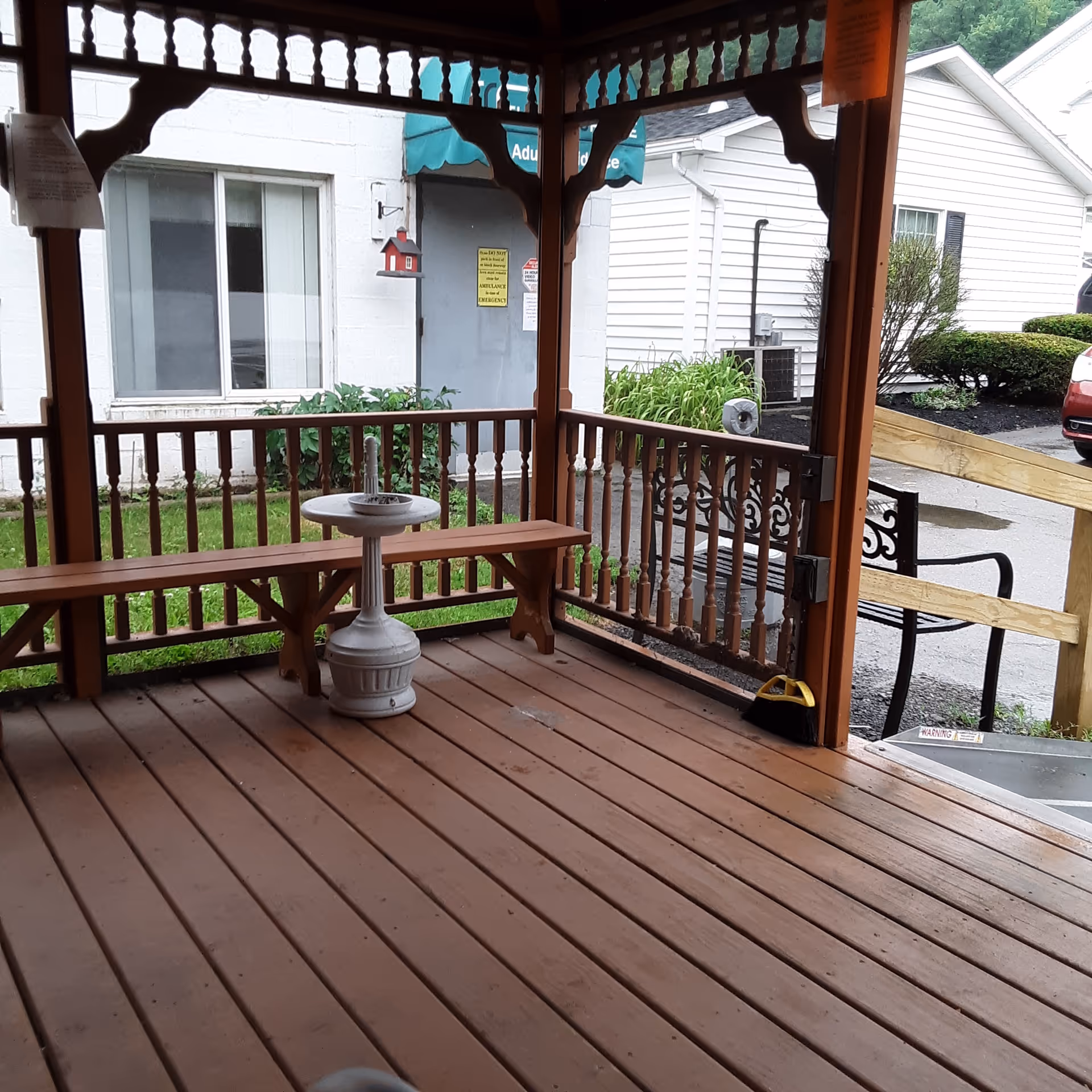 Wooden outdoor porch with benches and a round pedestal table by a white building.