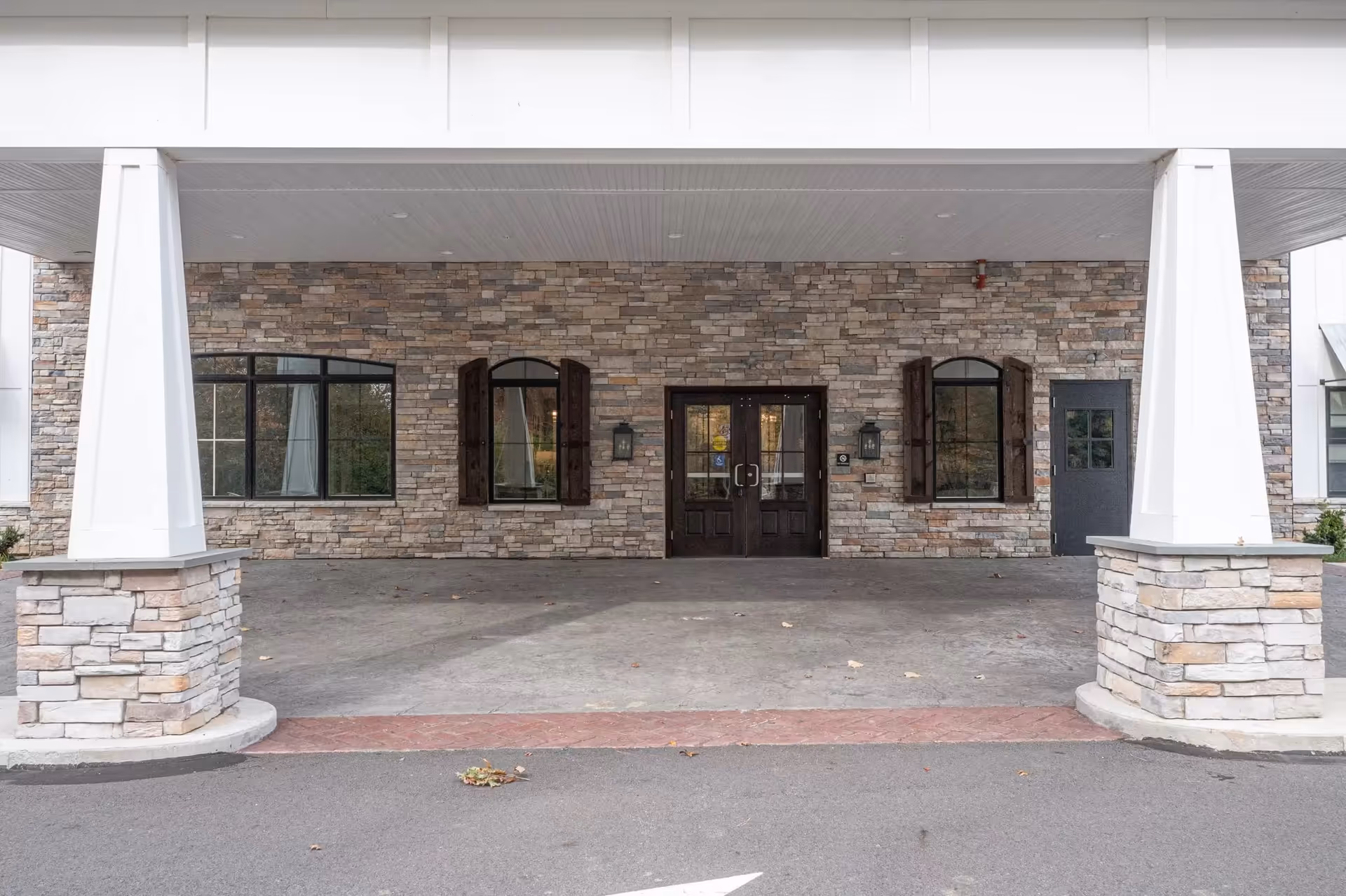 Covered entrance with stone facade, dark double doors, and two arched windows.