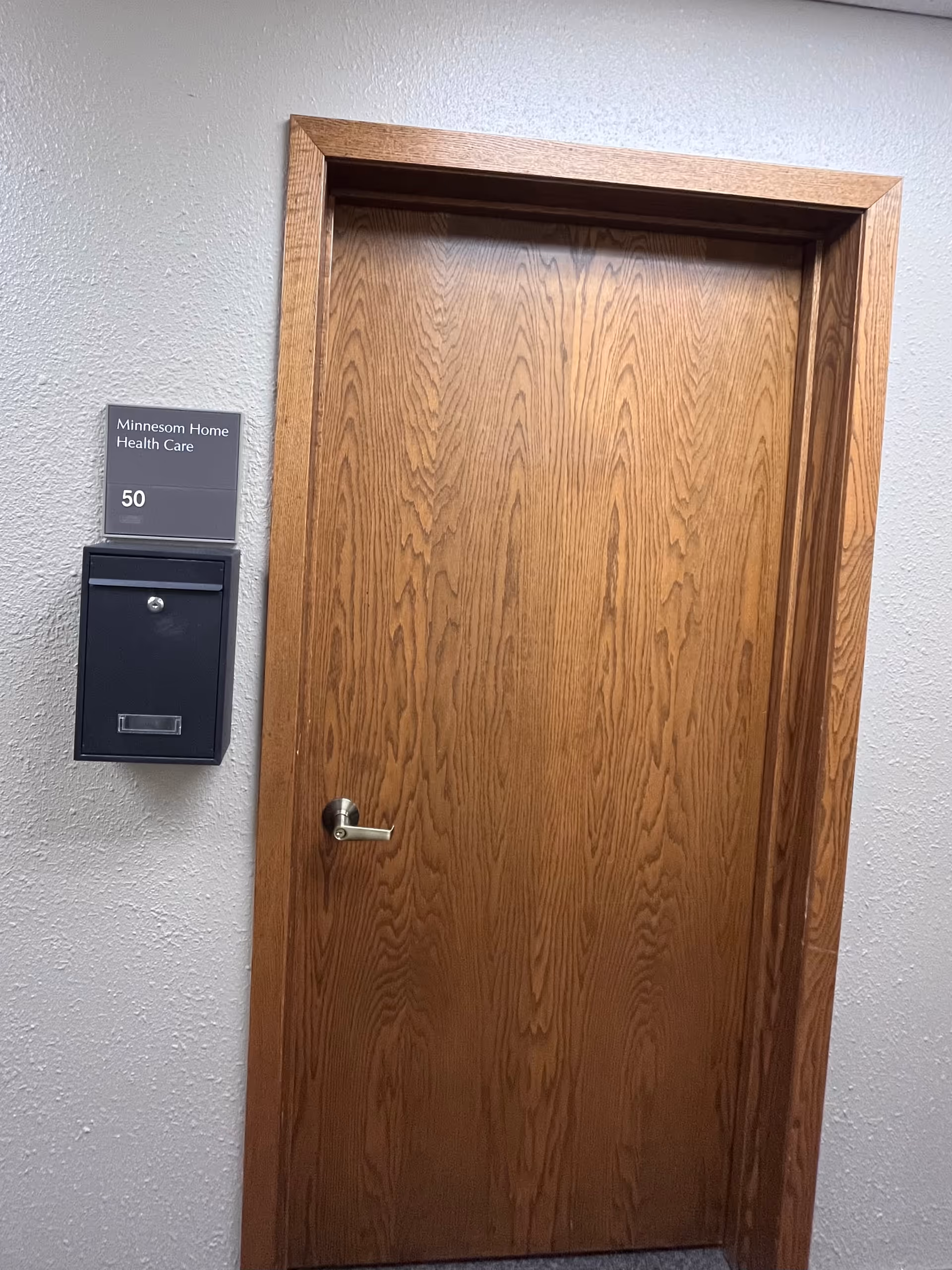 Interior hallway with a wooden door and Minnesom Home Health Care sign beside a mailbox.
