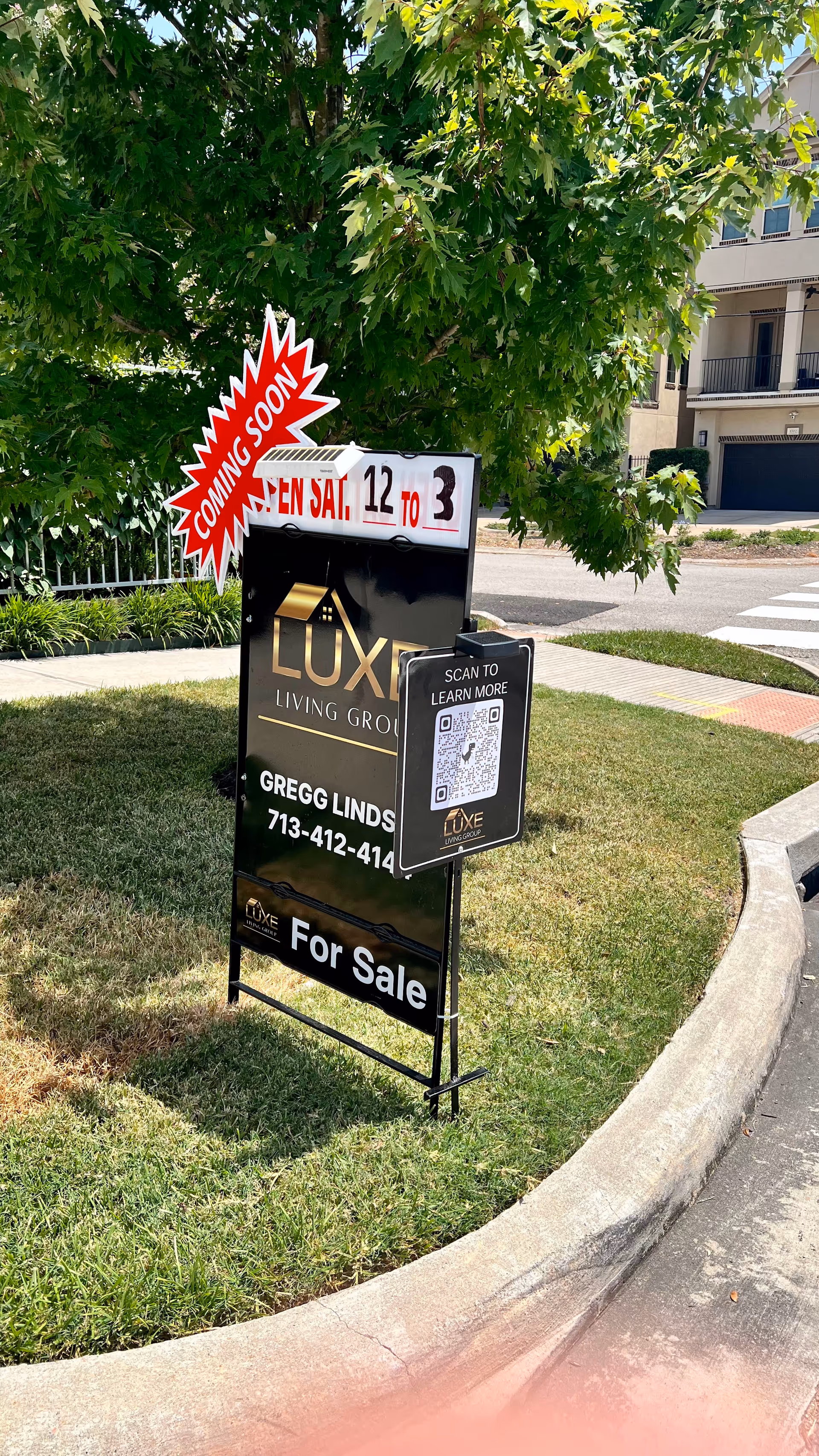 Outdoor lawn with a For Sale sign and QR card near a residential building.