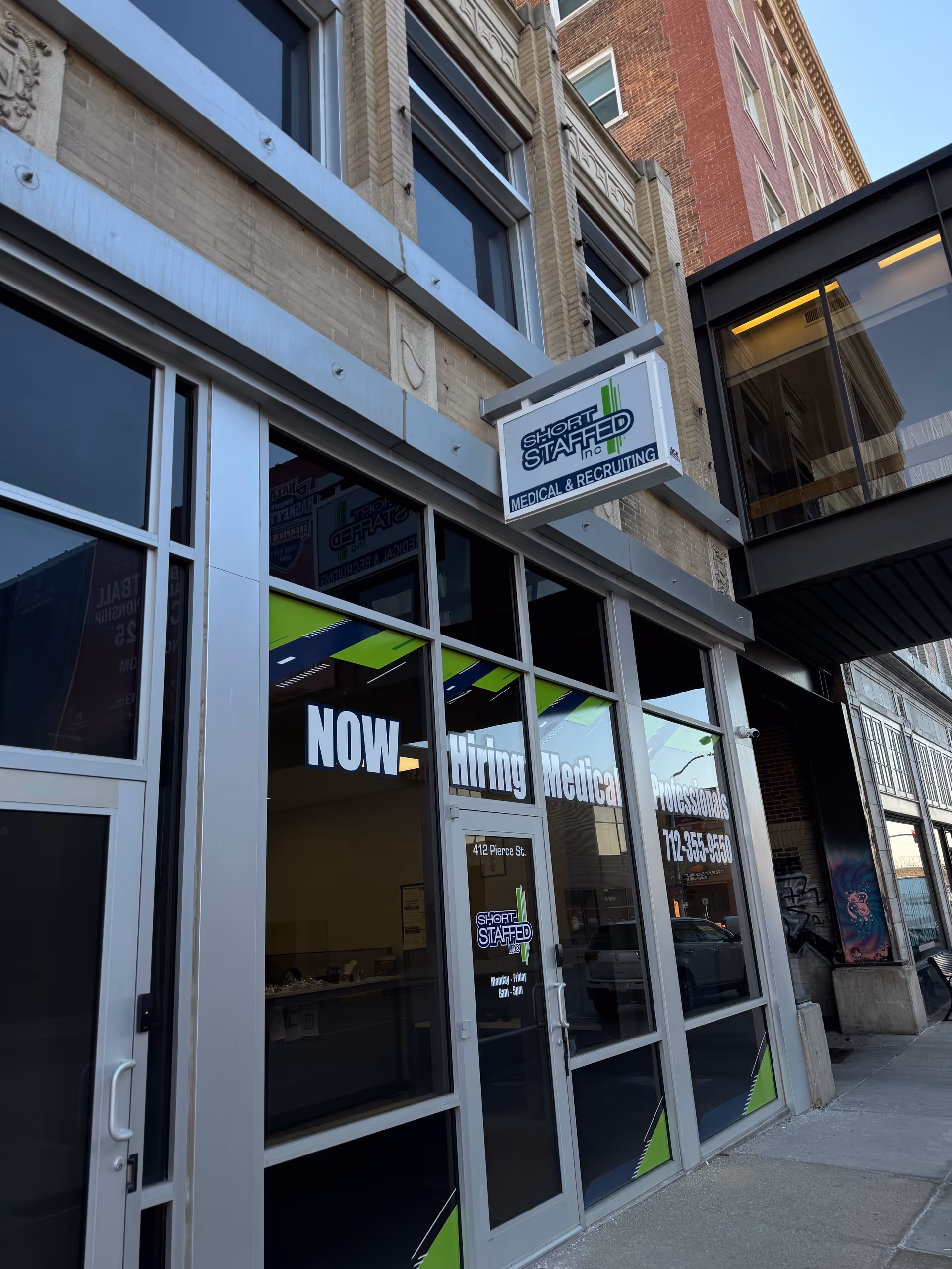 Exterior view of a storefront with Short Staffed Inc. medical staffing sign and Now Hiring windows.