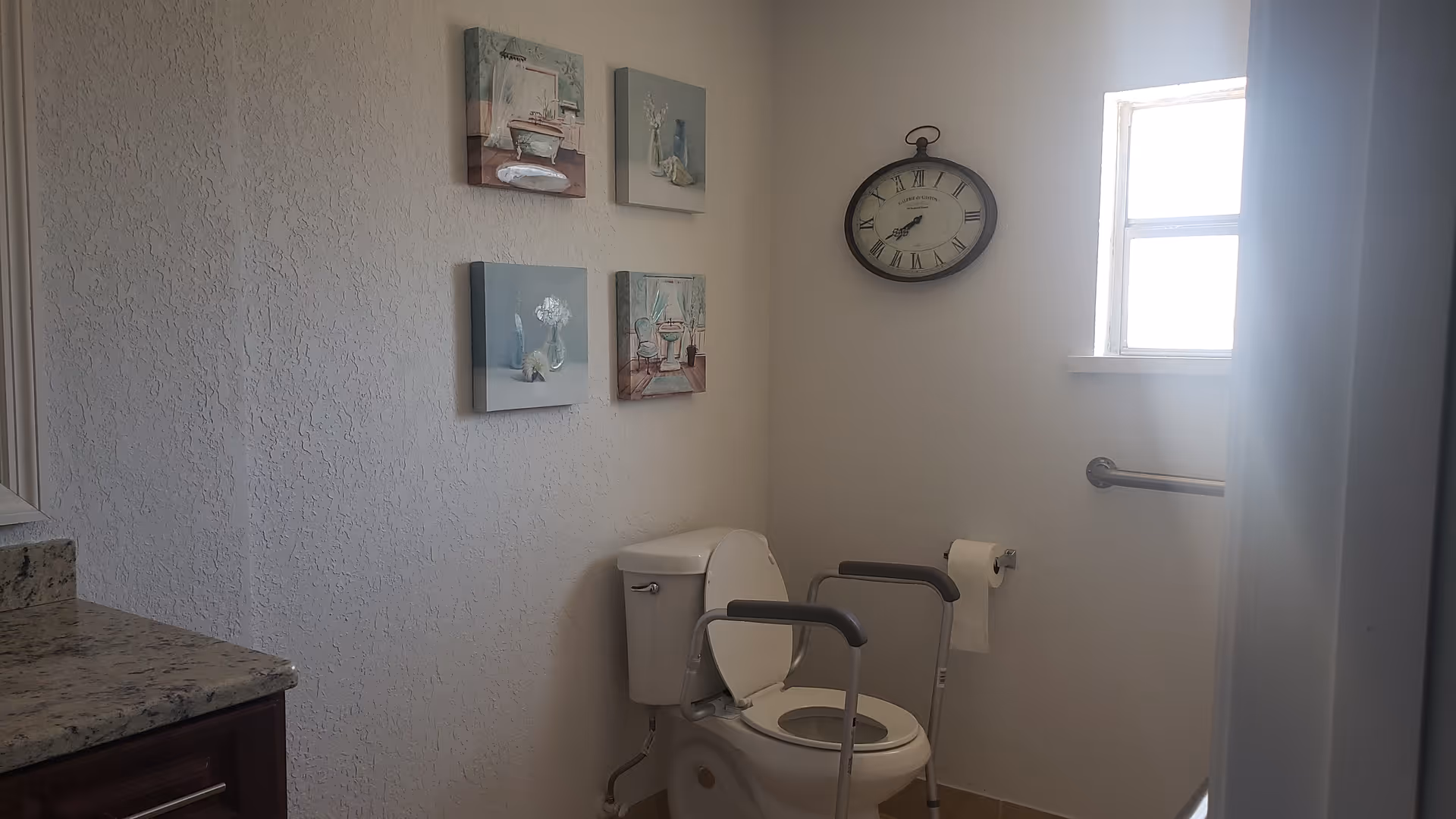 Accessible bathroom with toilet, grab bars, wall art, and a small window.