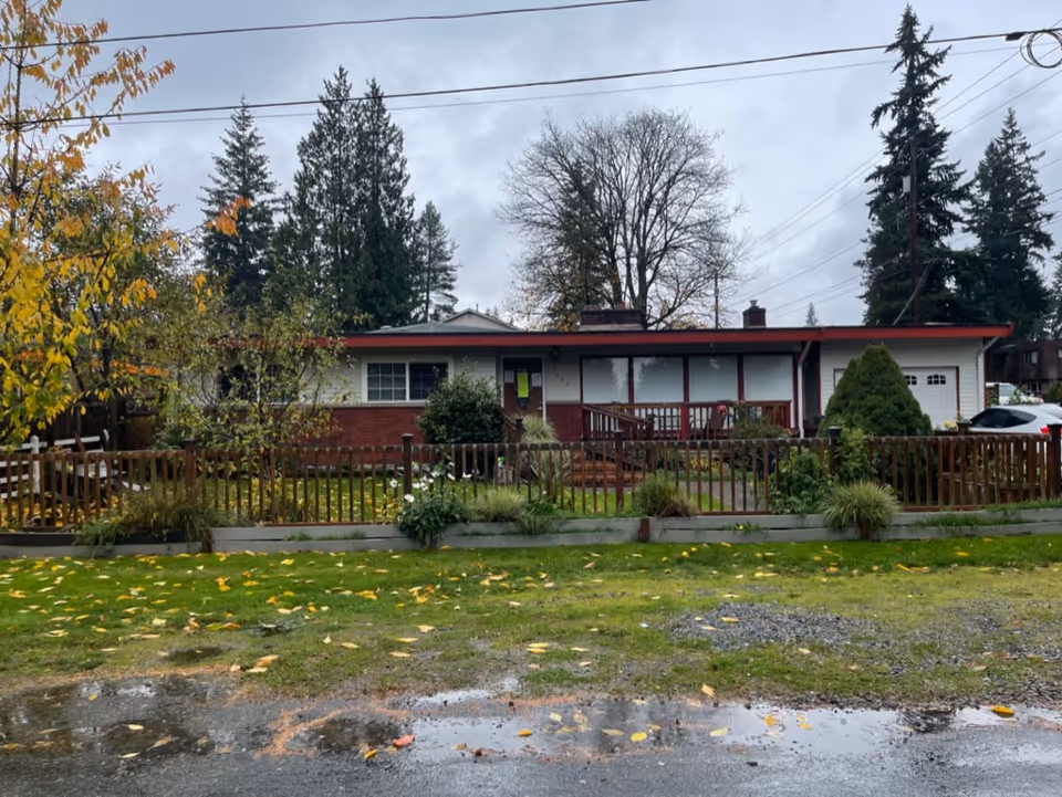 Single-story red brick home with a wooden fence, porch railing, and front yard.