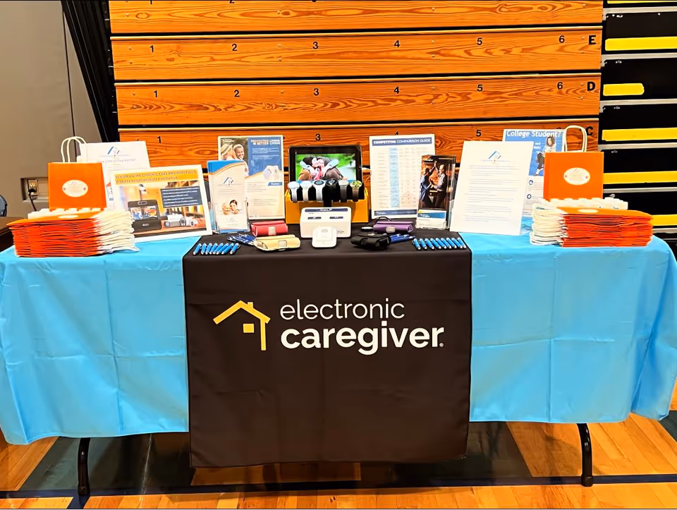 Information booth with brochures and a black Electronic Caregiver banner on a blue-clothed table.